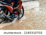 Small photo of Man ride motorcycle passing through flooded road. Riding motorbike on flooded road during flood caused by torrential rains. Flooded road with large puddle. Splash by motorcycle through flood water.