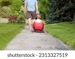 Small photo of Beautiful young girl sitting in a red wagon cart outdoors. Father is pulling a red wagon with his daughter.