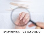 Small photo of We examine the nails on the female hand through a magnifying glass. Attention to the condition of nails and skin. Nearby are manicure items, orange tree sticks and a nail file
