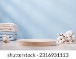 Small photo of Wooden round podium pedestal. Product presentation on blue background with cotton towels and branch of cotton