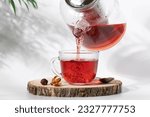 Hot tea is pouring from glass teapot into cup. Hibiscus red tea in glass cup close-up view
