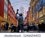Small photo of Bremen, Germany - November 30, 2018: bronze sculpture of a swineherd blowing a horn with pigs and dog in the pedestrian zone "Sogestrasse" with beautiful christmas decoration and lights at dawn
