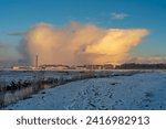 Small photo of Brake, Germany - January 18, 2024: cloud in scenic yellow sunlight over the factory REHAU, a mobile phone mast and the Kleiputte biotope on a snowy winter morning
