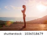woman doing yoga salutation to the sun Surya Namaskar exercises sequence asan at orange sun up morning high outdoor beautiful view of the island sky sea outside. Namaste hands full body place for text