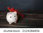 Small photo of Sad piggy bank and down arrow. Savings and reserves decrease. Inflation, depreciation of assets. Falling income, lower wages. Falling GDP. Economic recession, crisis. Capital flight, worsening economy