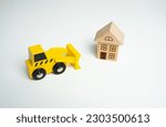 Small photo of Yellow toy bulldozer and a house. Encroachment on private property. Illegal buildings and construction. Violation of building codes. Demolition process.