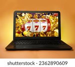 Small photo of Laptop on orange yellow background, casino winnings concept, 777 and bunch of coins flying on the screen
