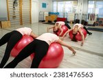 Two young girl laying on swiss balls and stretching their backs 