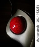 Small photo of A silver trackball mouse with a red ball with black spots on a black background