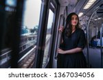 Portrait of a tall, slim, elegant and beautiful Indian Asian woman taking the train alone. She is leaning near the window and watching the scenery go by. The train is modern and clean.