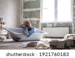Renovation apartment. Creative story young happy woman sits in bathtub in the middle of the room. Empty walls, repairs house with their own hands.