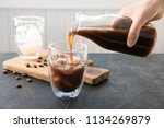 Woman pouring cold brew coffee into glass on table