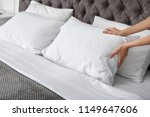 Young woman plumping white pillow on bed, closeup