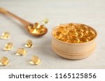 Bowl and spoon with cod liver oil pills on light background