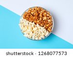 Different kinds of popcorn in bowl on color background, top view