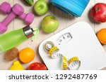 Flat lay composition with scales, healthy food and sport equipment on wooden background. Weight loss