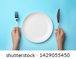 Woman with fork, knife and empty plate on color background, top view