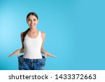 Attractive young woman with slim body wearing her old big jeans on color background. Space for text