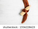 Shampoo bottle wrapped in lock of hair on white wooden background, flat lay with space for text. Natural cosmetic products