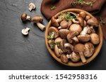 Different fresh wild mushrooms in bowl on black background, flat lay
