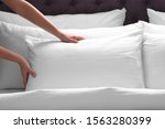 Woman fluffing white pillow on bed, closeup