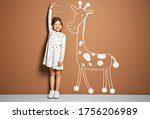Little girl measuring height and drawing of giraffe near brown wall