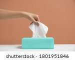 Woman taking paper tissue from box on light brown background, closeup