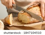 Woman cutting freshly baked bread at wooden table, closeup