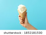 Woman holding waffle cone with delicious ice cream on light blue background, closeup