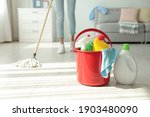 Woman washing floor with mop at home, focus on bucket and cleaning supplies