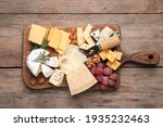 Cheese plate with grapes and nuts on wooden table, top view