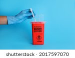 Doctor throwing used syringe into sharps container on light blue background, closeup