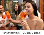 Friends spending time together, focus on young woman drinking Aperol spritz cocktail