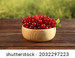 Fresh ripe red currant in bowl on wooden table outdoors