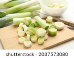 Fresh raw leek slices and knife on white wooden table, closeup