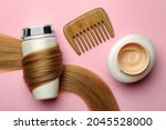 Small photo of Bottle wrapped in lock of hair, jar and comb on pink background, flat lay. Natural cosmetic products