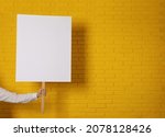 Woman holding blank sign near yellow brick wall, closeup. Space for design