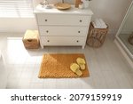 Small photo of Stylish orange mat with slippers near chest of drawers in bathroom