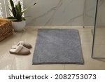 Small photo of Soft grey bath mat and slippers on floor indoors
