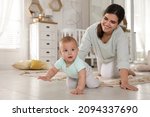 Small photo of Happy young mother watching her cute baby crawl on floor at home