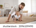Small photo of Happy young father watching his cute baby crawl on floor at home