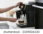 Woman using modern espresso machine for making coffee with milk in kitchen, closeup