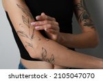 Woman applying cream on her arm with tattoos against light background, closeup