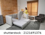 Young woman unfolding sofa into a bed in room. Modern interior
