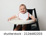 Small photo of Cute little baby wearing bib in highchair on white background