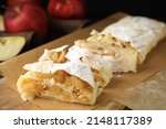 Delicious apple strudel with almonds and powdered sugar on wooden board, closeup