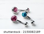 Stylish navel barbells on white wooden table, closeup. Piercing jewelry