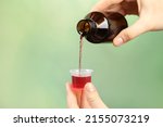 Woman pouring cough syrup into measuring cup on light green background, closeup