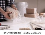 Small photo of Man covering box with bubble wrap at table in warehouse, closeup