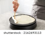 Woman cooking delicious crepe on electric pancake maker at table indoors, closeup